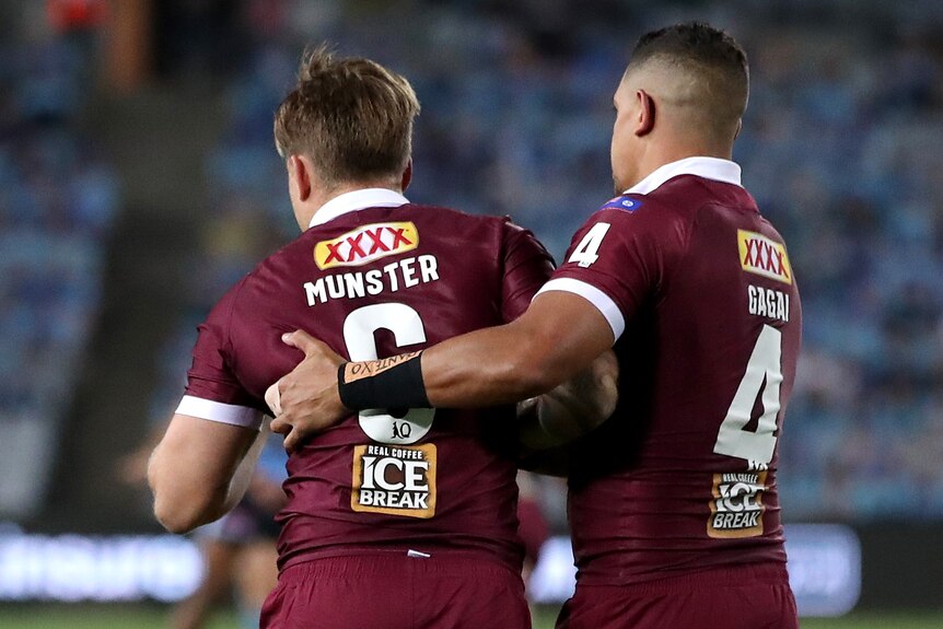 Cameron Munster of the Maroons is helped up by Dane Gagai during a State of Origin game.