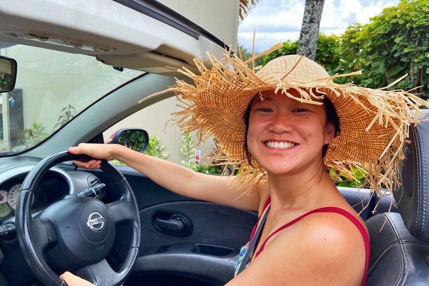 An Asian woman smiling while driving with a beige hat 