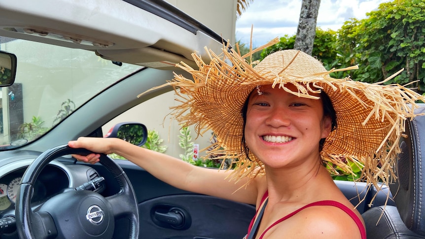 An Asian woman smiling while driving with a beige hat 