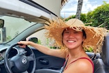 An Asian woman smiling while driving with a beige hat 