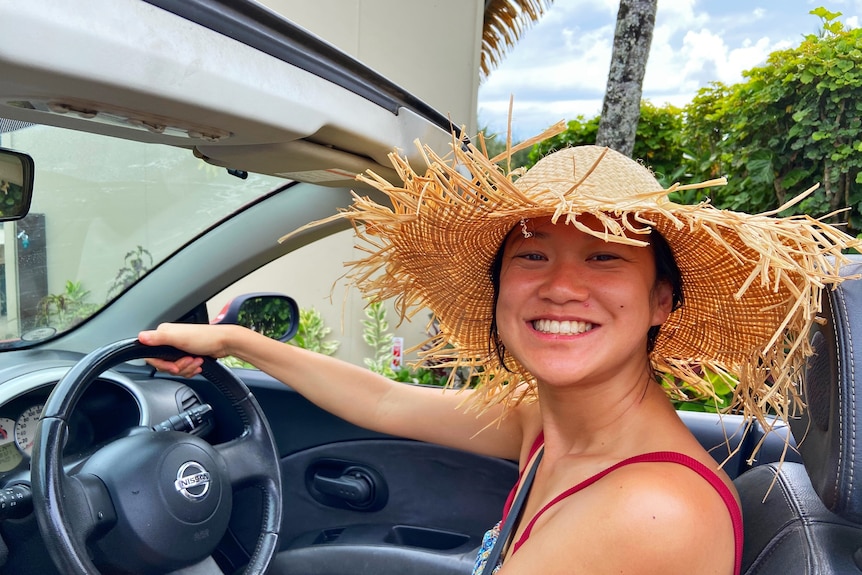 An Asian woman smiling while driving with a beige hat 