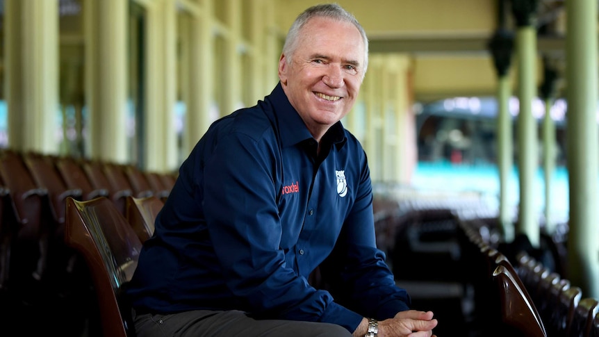 A former Australian cricket captain smiles at the camera from his seat in the stand at the SCG.