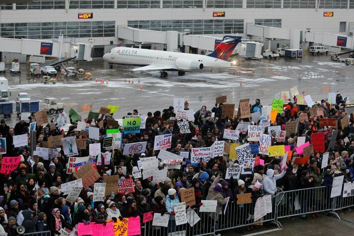 Protesters stand on the tarmac holding signs in Michigan.