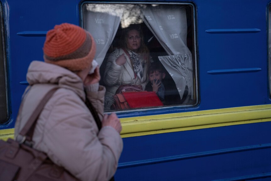 An exterior shot of someone outside a train, looking through a train window to a woman and a young boy.