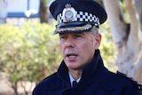 A police officer, in full uniform, including a hat, speaking.