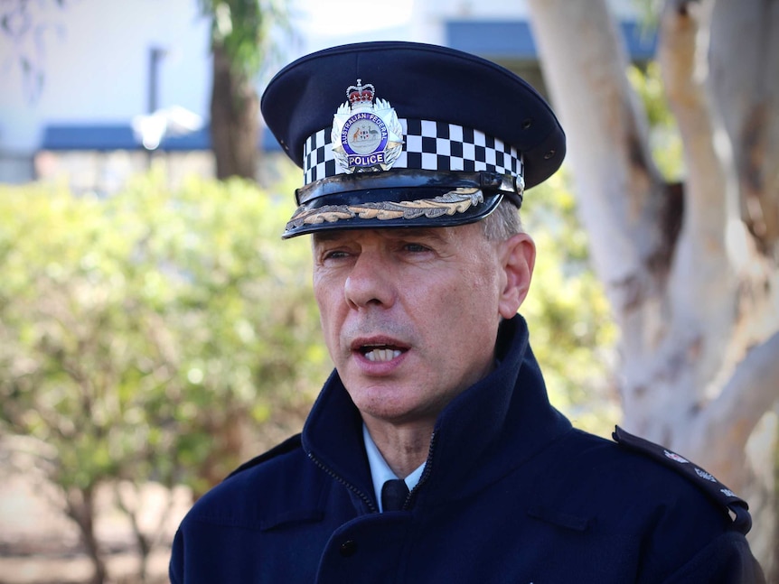 A police officer, in full uniform, including a hat, speaking.