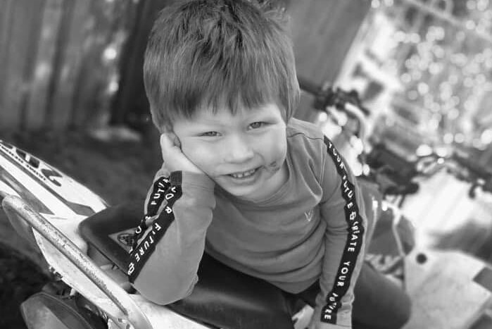 A black and white photo of a boy smiling and posing on a quad bike