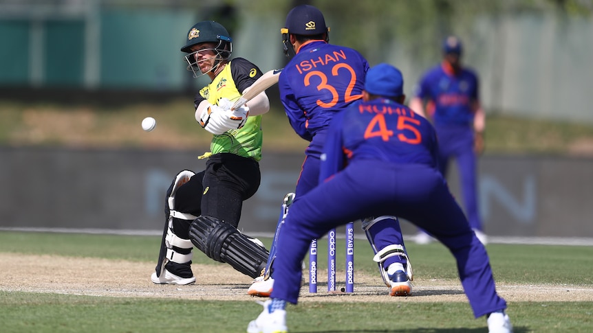 Australia batter David Warner plays a reverse sweep as Ishan Kishan and Rohit Sharma of India react in the field.