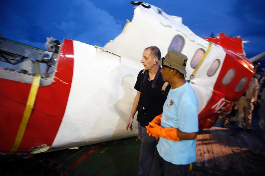 Investigators walk near a section of the tail of AirAsia Flight QZ8501