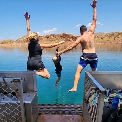 A woman, a child and a man jump into the ocean. Seen from the back. 