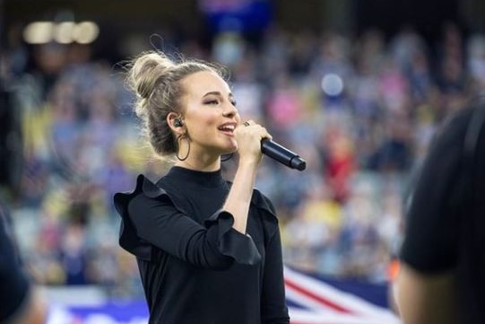 A performer stands, a microphone in her hand, singing in a stadium.