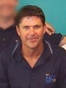 A dark-haired young man in a branded polo shirt.