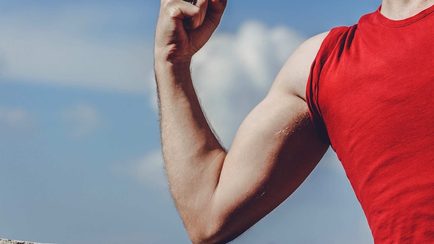 Close-up of man's arm flexing, with the blue sky in the background.