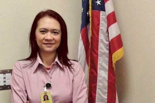 A woman in a pink shirt stands next to a red and white flag