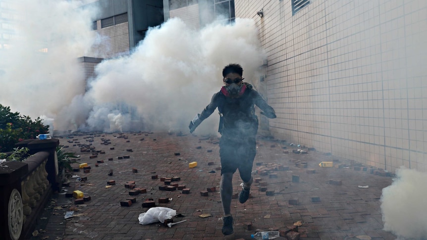 A protester is attempting to escape the university campus, with clouds of tear gas behind him.