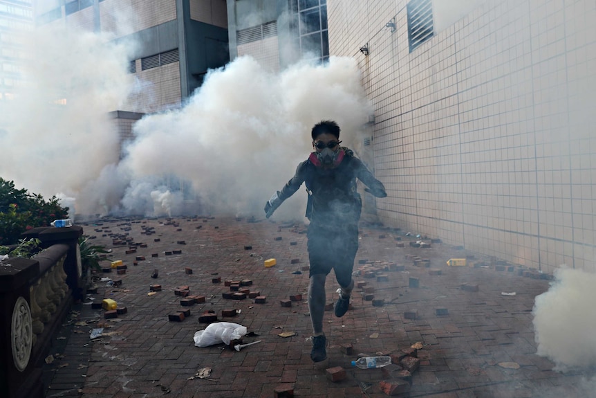 A protester is attempting to escape the university campus, with clouds of tear gas behind him.