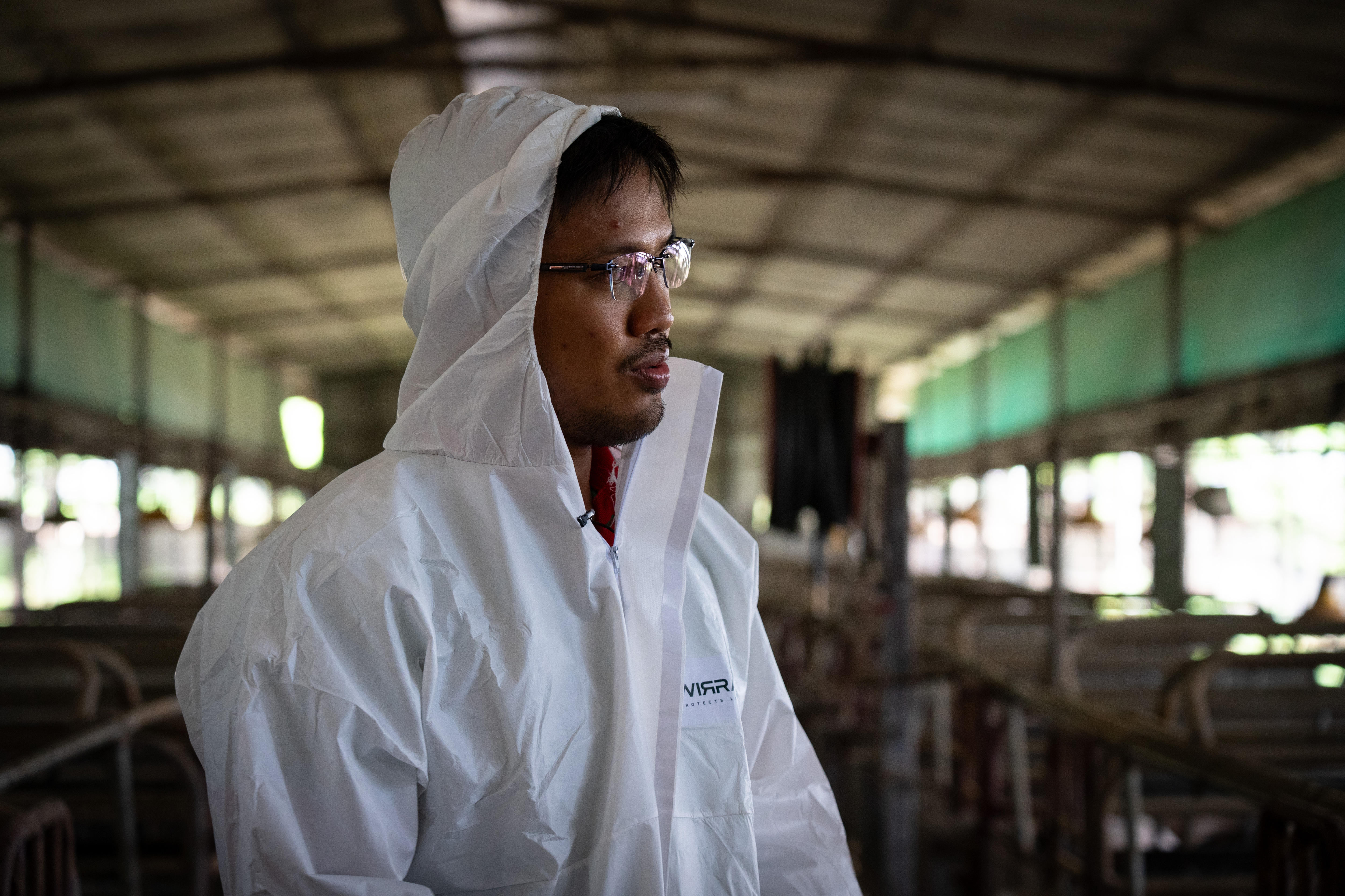 A man in a white lab coat stands inside a shed with light streaming through the windows