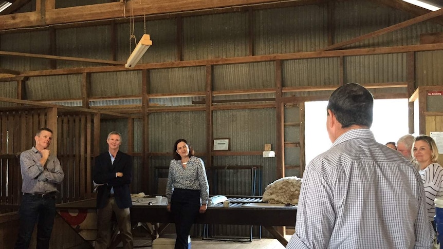 Premier Annastacia Palaszczuk standing in woolshed talking with a semicircle of graziers.
