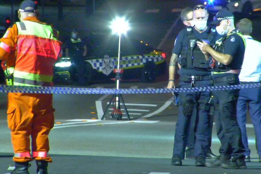 Emergency services workers, including uniformed SES and police officers, stand at a taped-off crime scene.
