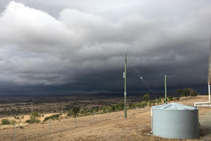 Dark storm clouds roll in over a dry grass paddock