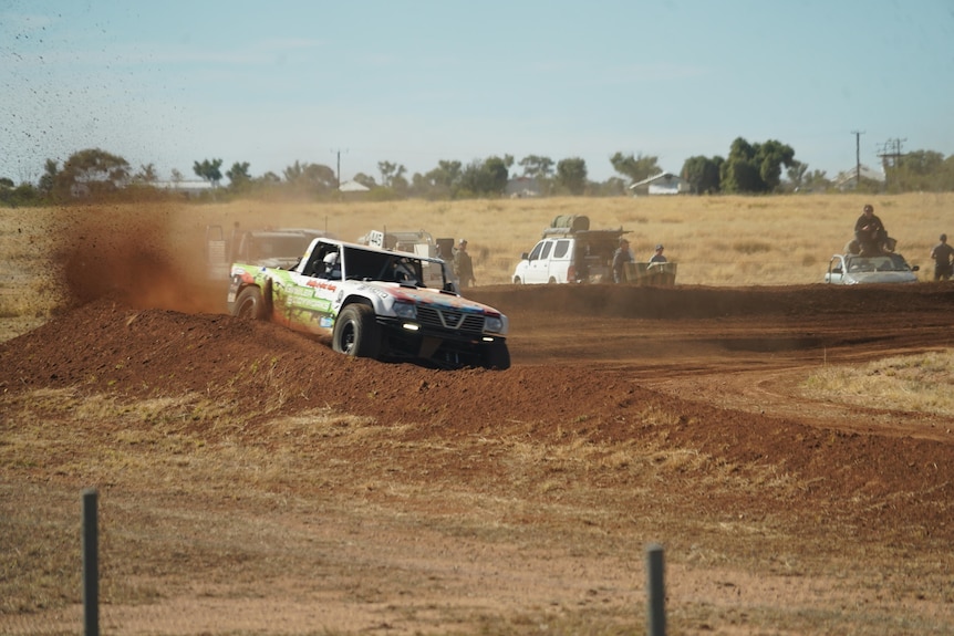 truck kicking up dirt as it takes on a tight bend on a race track