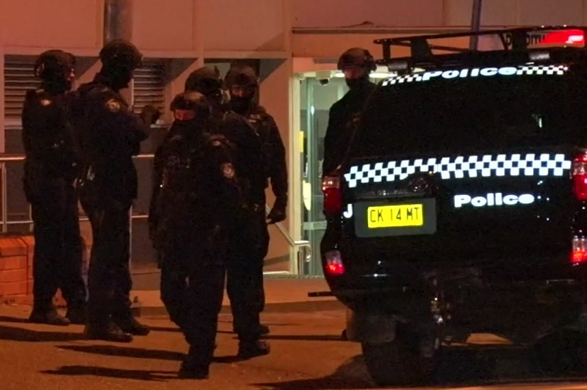 Six police officers are seen standing next to a black police vehicle on the street.