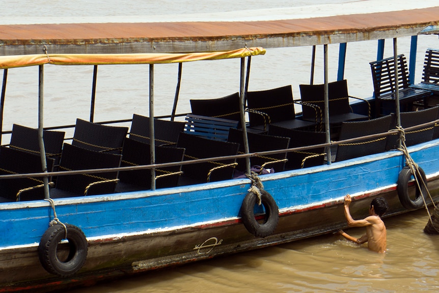 A Vietnamese man washes a tourist boat in the Mekong River.