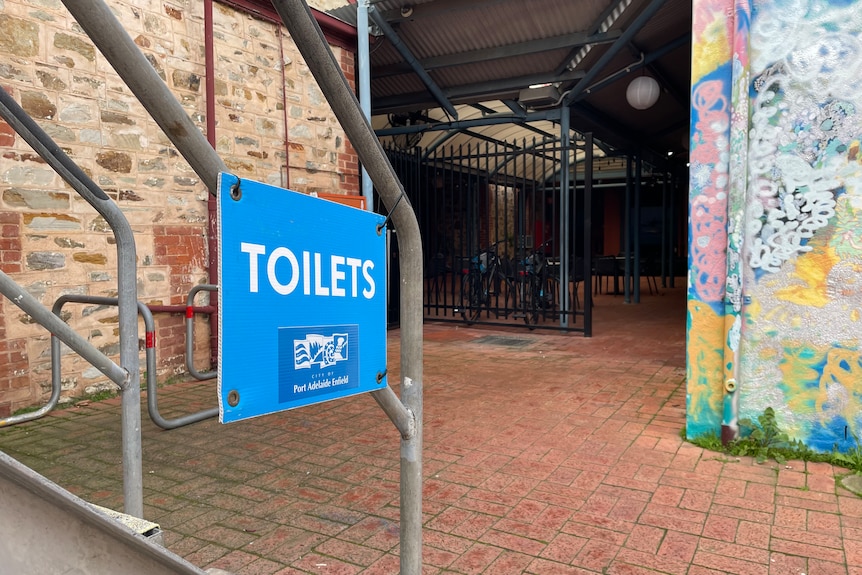 A blue sign reading TOILETS hangs from a stair rail