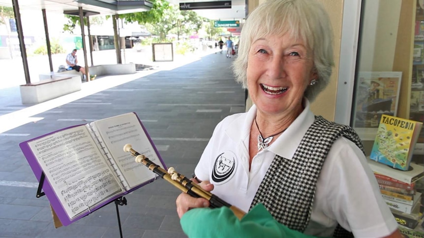 Older woman stands in the street busking using a set of small bagpipes