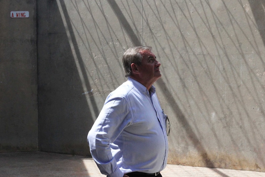 A man stares up at the sky inside a concrete cell block.