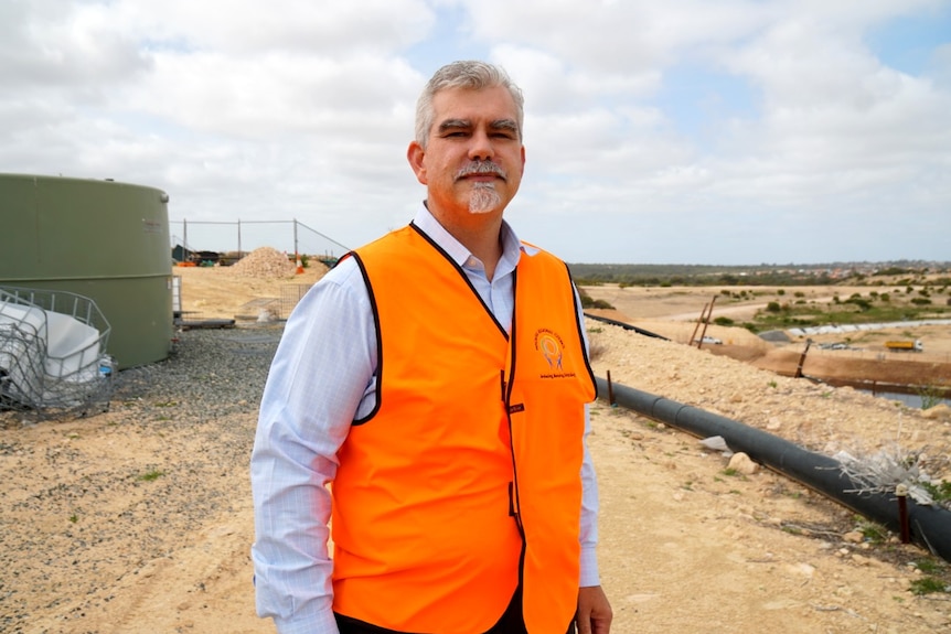 A man wearing a bright orange vest stands in front of a rainwater tank at a rubbish processing facility.
