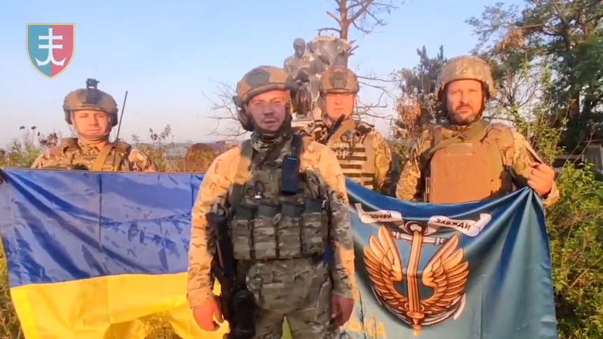 Ukrainian soldiers stand with Ukrainian flag.