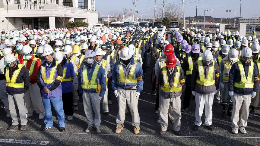 Rows of decontamination workers stand with their heads bowed.