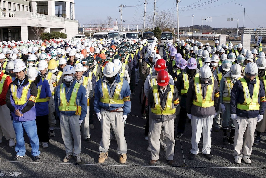 Rows of decontamination workers stand with their heads bowed.