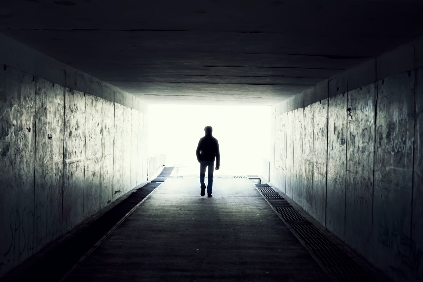 A man walking into the light at the end of a dark tunnel