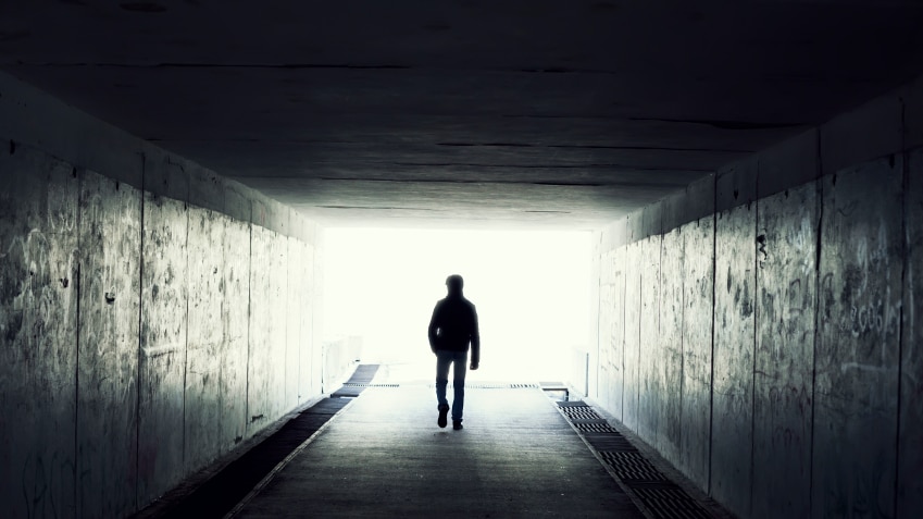 A man walking into the light at the end of a dark tunnel