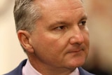 Chris Bowen looks into the distance at a press conference with autumn colours behind him