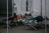 Patients on stretchers receiving oxygen from cylinders in a temporary medical tent.