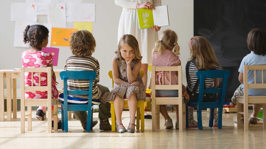 children sitting on chairs with one girl facing the opposite direction looking unhappy 
