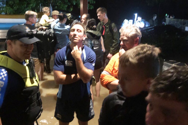 A group of residents with police and other authorities stand in street in flooded Townsville.