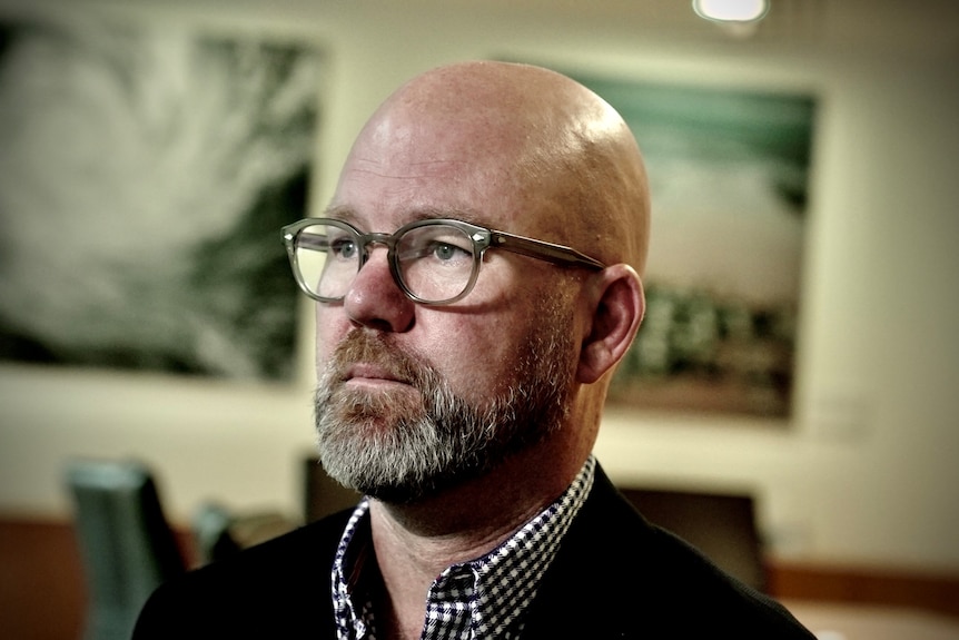 A bald man with a beard and glasses looks off into the distance.
