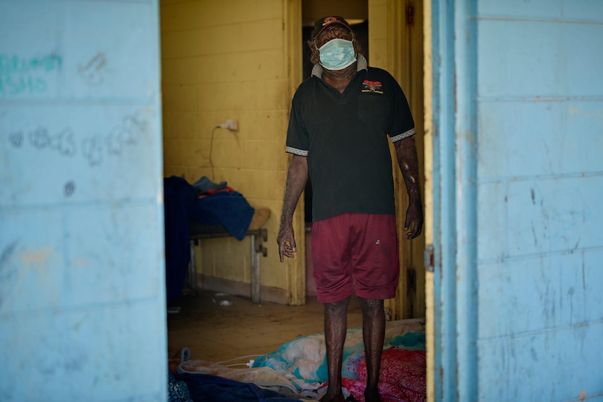 A man stands in a doorway wearing a mask. 