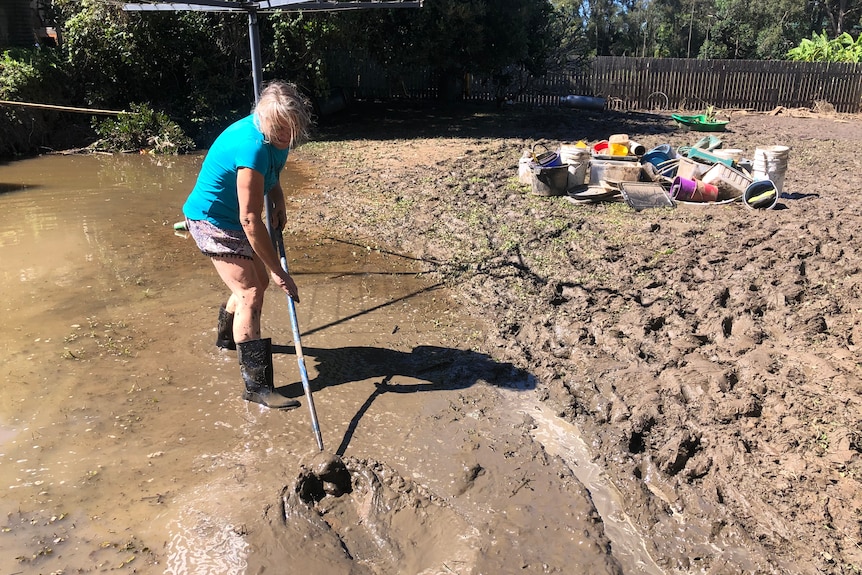 A woman who lives on the Hastings River in Port Macquarie shovelling mud from her backyard.