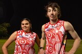 An indigenous man and woman wearing a red and white football jersey with their hands on their hips.
