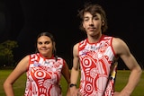 An indigenous man and woman wearing a red and white football jersey with their hands on their hips.