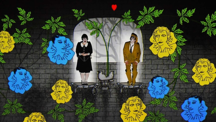 Two singers stand on platforms surrounded by leaves and flowers.
