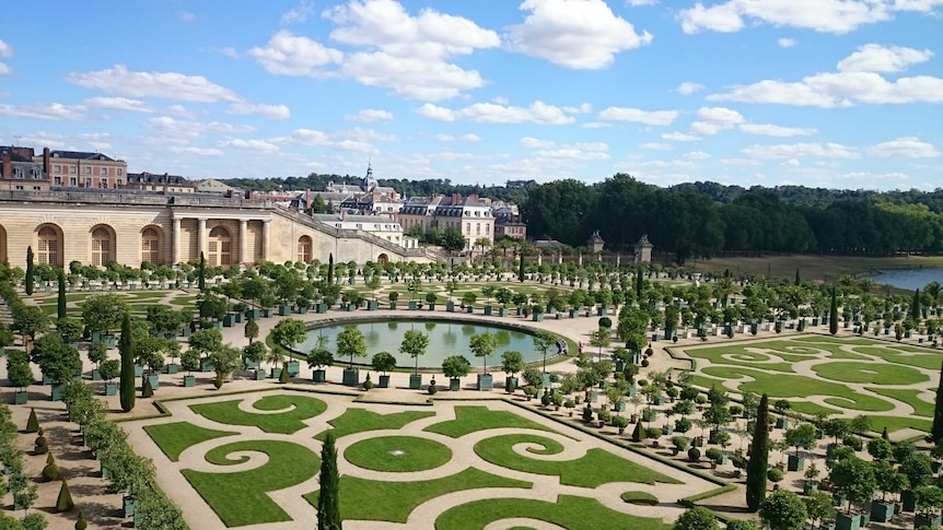 Ornate trees, lawns and ponds in the Orangerie Gardens at Versailles, with a view to the town in the distance.