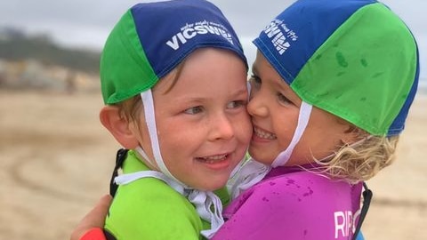 Two children in swimmers hug on a beach.