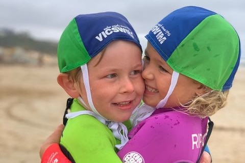 Two children in swimmers hug on a beach.