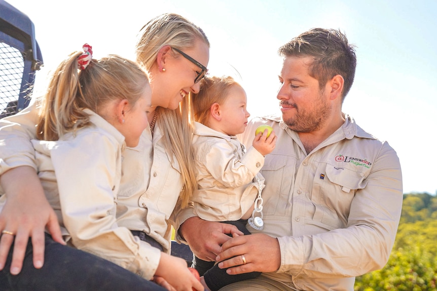 A mum, dad and their two kids sit on the back of a quad bike laughing.